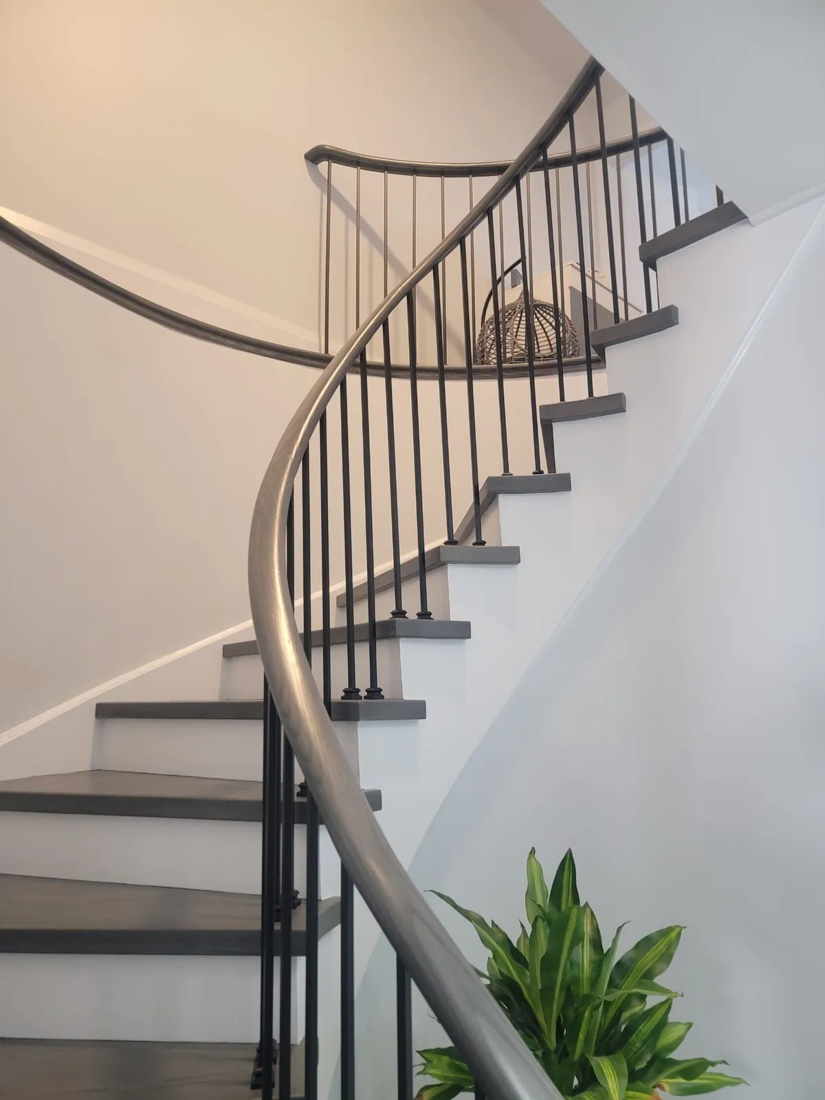 Curved stair with gray treads and a dark iron railing.