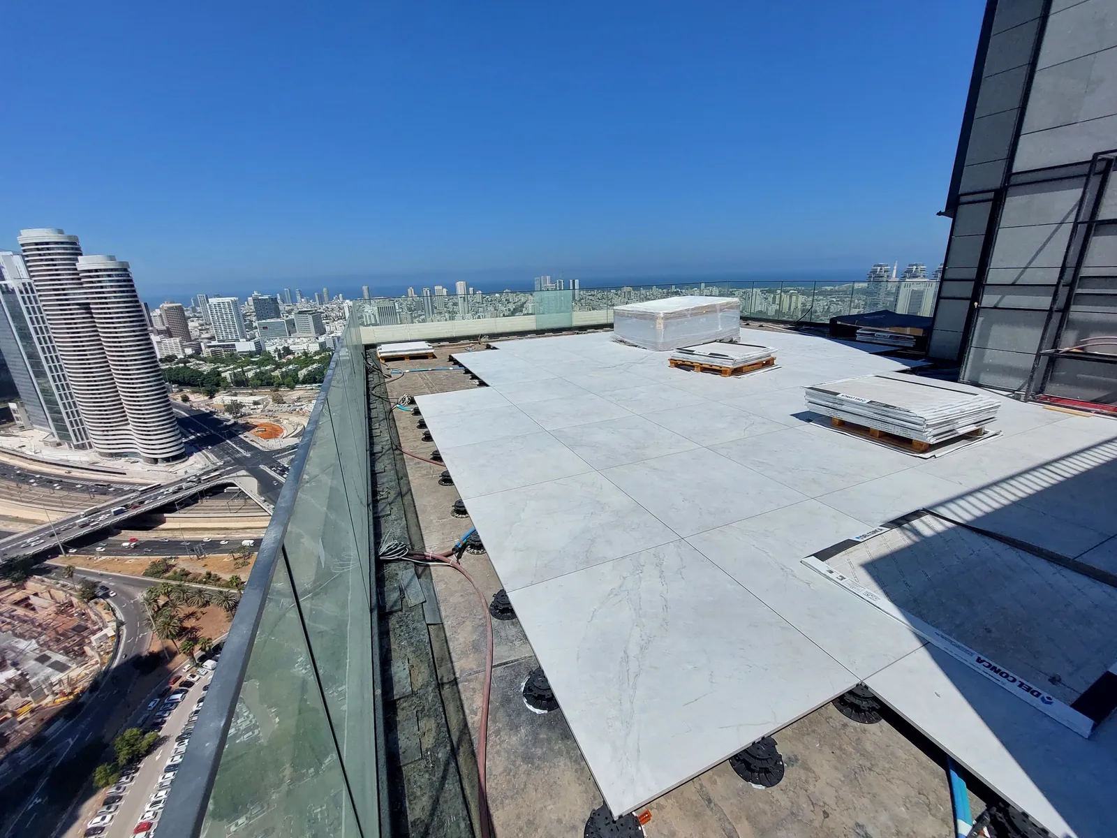 High-rise rooftop deck of large porcelain pavers under a blue sky.
