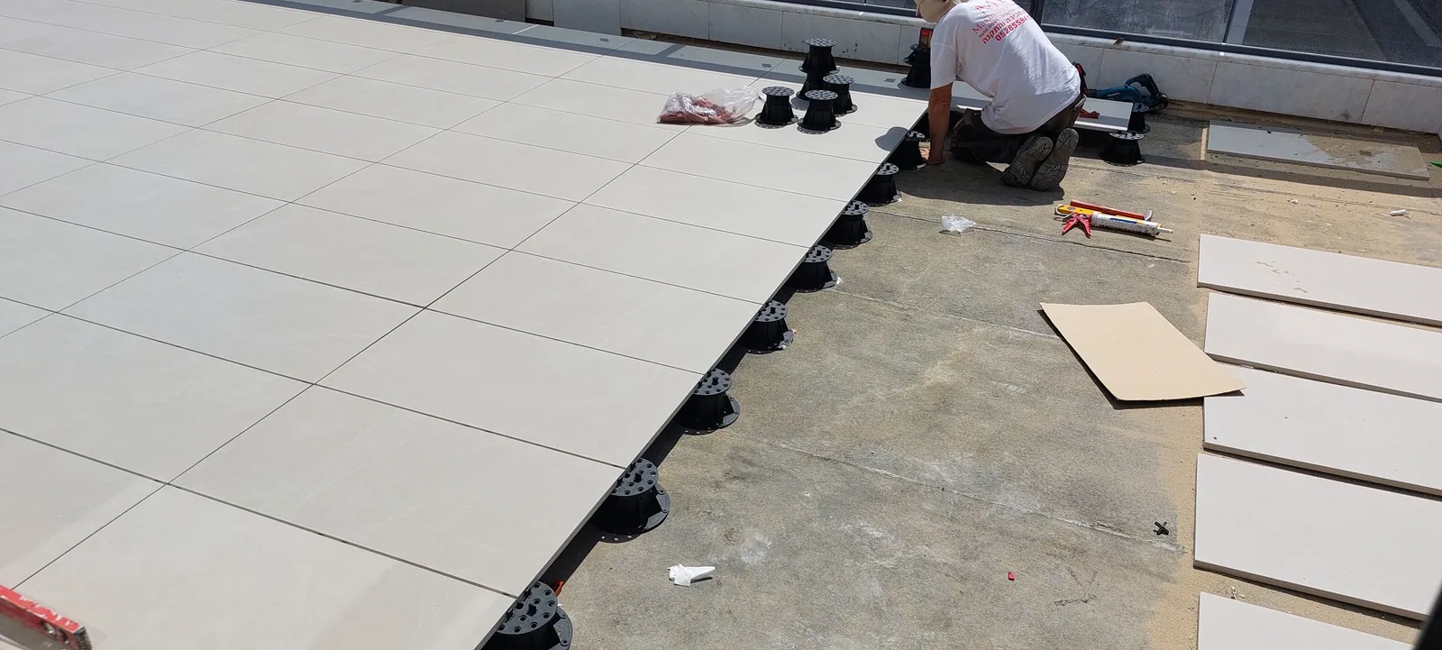 Installer setting pavers on pedestals along a roof edge.