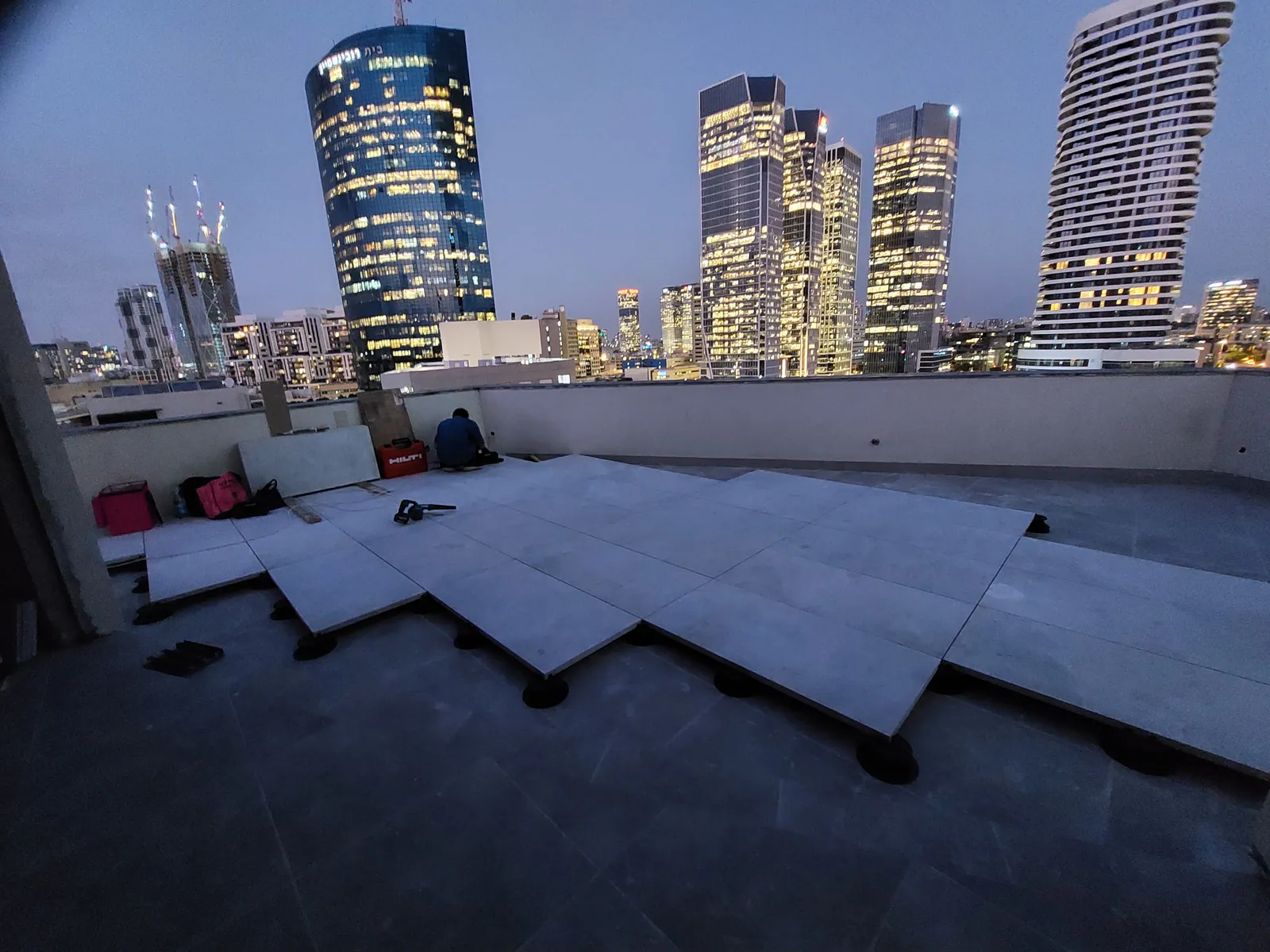 Rooftop pavers going down at dusk with the city skyline behind.