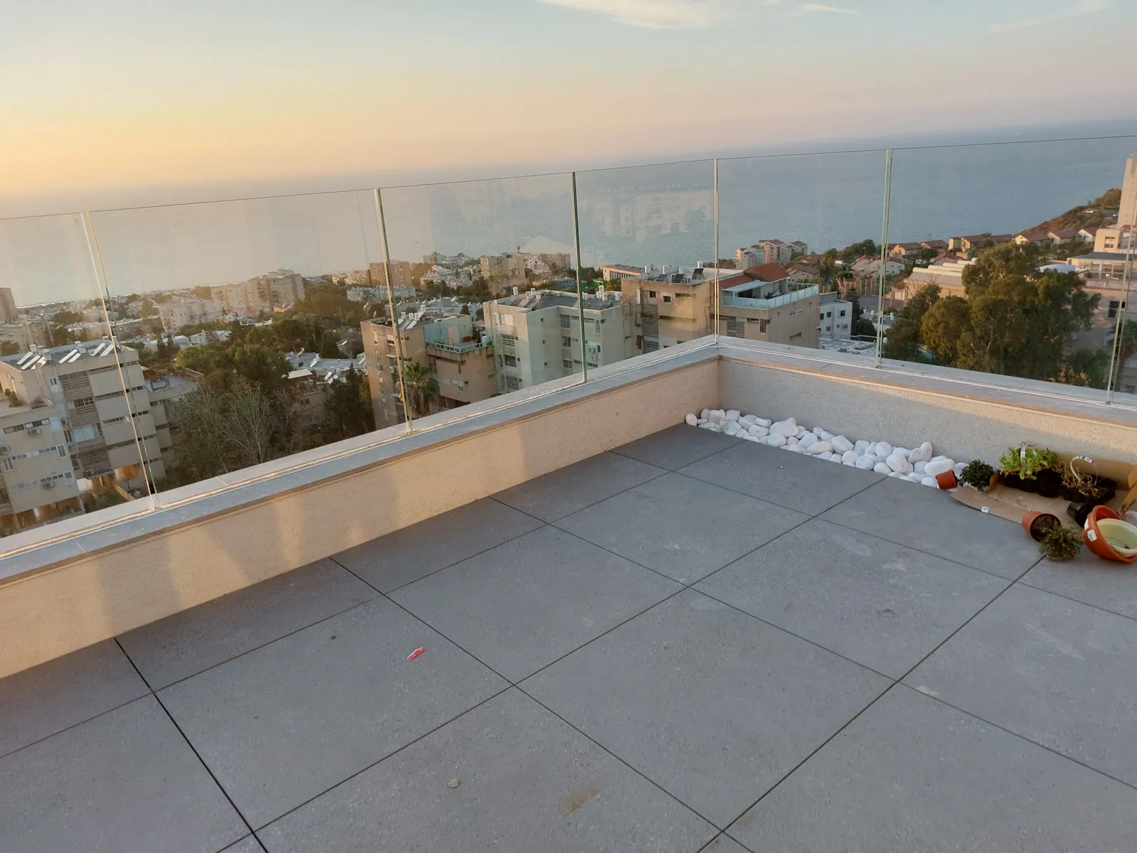Finished porcelain paver terrace with glass railing at sunset.